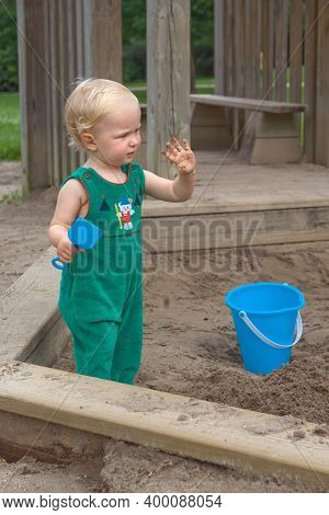 Child Baby In Sandbox Playing With Beach Toys. Girl Toddler Watching Exploring Sand On Hands. Kid Ha