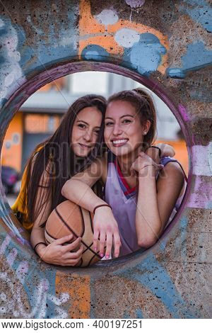 Two Funny Caucasian Girls In Sportswear Pose With The Ball. They Are Leaning On A Hole.