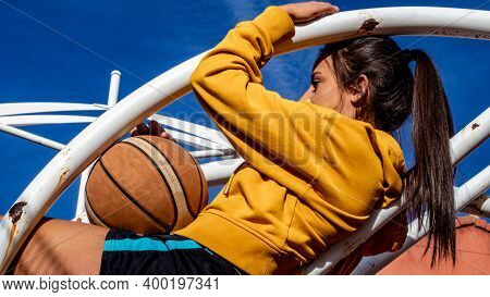 The Basketball Player Wearing A Yellow Sweatshirt Stands On A Basket While Holding The Ball In Her L
