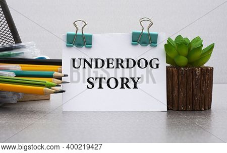 Underdog Story - Words On A White Sheet With Clamps Against The Background Of A Cactus And Jars With