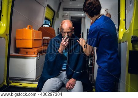 Injured Man In A Blanket Is Getting First Aid In An Ambulance Car.