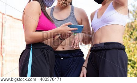 Three Cheerful Girls Wearing Masks Look At A Picture Of A Mobile Phone While Practicing Basketball O