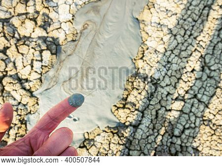 Persons Hand With Muddy Finger Next To Mud Volcanoe In The Background