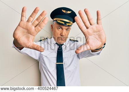 Handsome middle age mature man wearing airplane pilot uniform doing frame using hands palms and fingers, camera perspective 