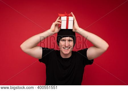 Photo Shot Of Handsome Positive Smiling Adult Man Isolated On Red Background Wall Wearing Black Hat 
