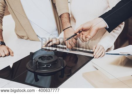 Close Up Manager In Suit Is Showing Kitchen Burner To Couple Clients In Kitchen Store. Young Couple 
