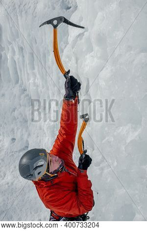 Alpinist Man With Ice Tools Axe Climbing A Large Wall Of Ice. Outdoor Sports Portrait.