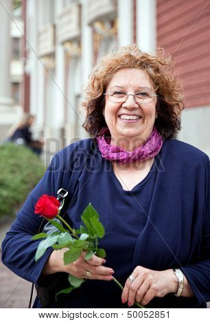 happy smiling senior lady, holding rose outdoors