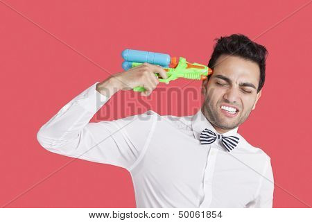 Frustrated man holding toy gun to his head over red background