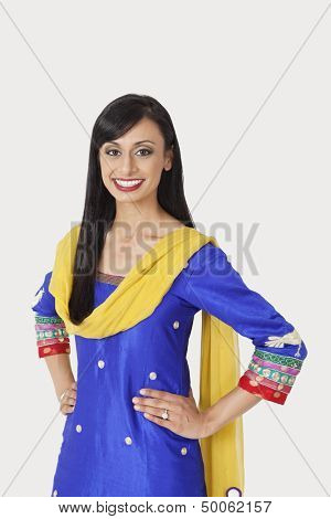 Portrait of beautiful Indian woman in traditional wear standing with hands on hips over gray background