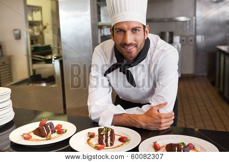Happy chef looking at camera behind counter of desserts in a commercial kitchen