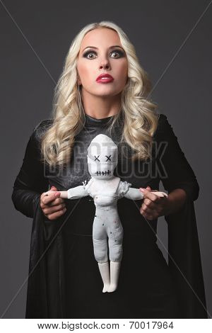 Witch holding a voodoo doll. Costume for Halloween Party. Blond witch.
