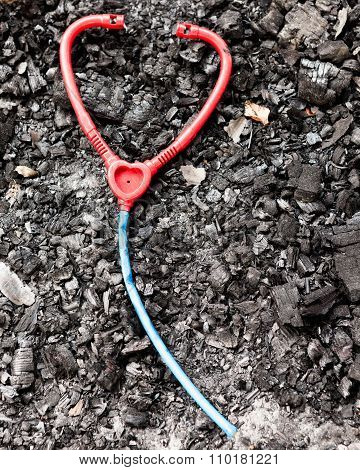 Plastic toy stethoscope on burned ground