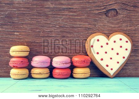 some appetizing macarons with different colors and flavors and a homemade heart-shaped cookie on a blue wooden surface, against a rustic wooden background