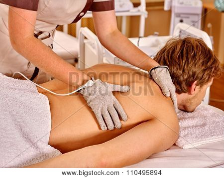 Strong man receiving back electric massage at beauty salon. Beautician wearing electricity gloves. 