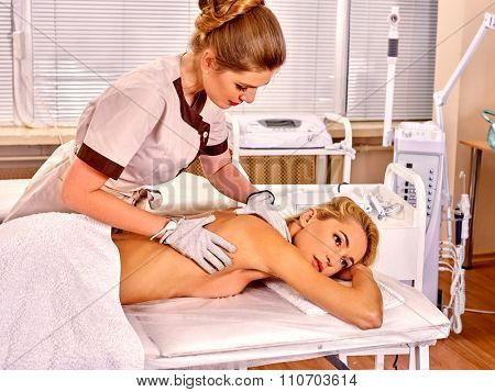 Young blond beauty woman  receiving electric massage at beauty salon. Beautician wearing electricity gloves. Interior with  device for hardware cosmetology. 