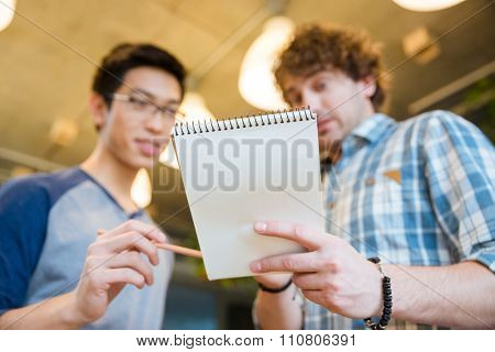 Student showing his notes in notepad to his friend