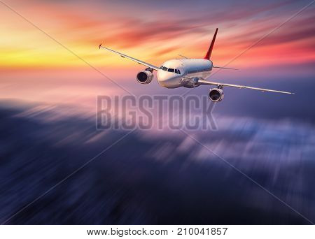 Modern airplane mith motion blur effect is flying over low clouds at sunset. Landscape with passenger airplane, blurred clouds, sunlight in dusk. Passenger aircraft. Business travel. Commercial plane