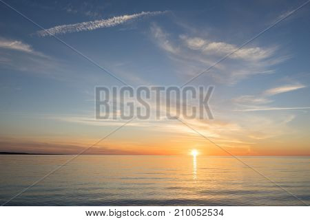 Evening sunlight on coast pink clouds blue sky reflection on water. Beach in summer. Seaside natural environment. Shore in Kesselaid small island in Estonia. Nature Reserve in North Europe