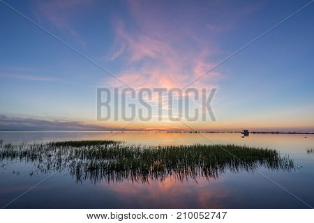 Evening sunlight on coast pink clouds blue sky reflection on water. Beach in summer. Seaside natural environment. Shore in Kesselaid small island in Estonia. Nature Reserve in North Europe