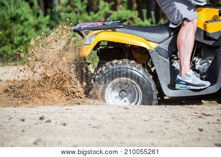 An Atv Quadbike Get Stuck In A Sandy Road Near Forest And Having Wheel-spin Making A Spray Of Sand