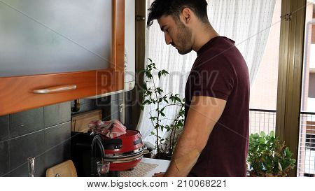 Young attractive man preparing a cup of espresso coffee with machine at home then drinking it