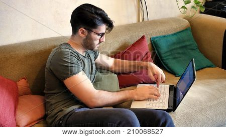 Attractive Young Man with Serious Expression, with Laptop on Couch, Working on his Start-up Business - Young Male College or University Student Doing Homework on Sofa