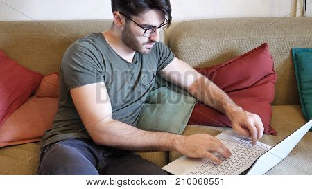 Attractive Young Man with Serious Expression, with Laptop on Couch, Working on his Start-up Business - Young Male College or University Student Doing Homework on Sofa