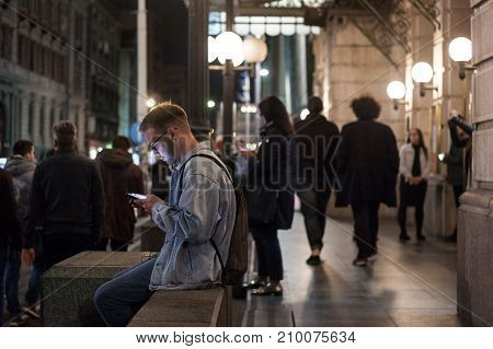 BELGRADE SERBIA - OCTOBER 14 201: Young white man using his smartphone at night in Belgrade a woman doing the same in the background. Serbia is one of the most phone equipped countries in Balkans