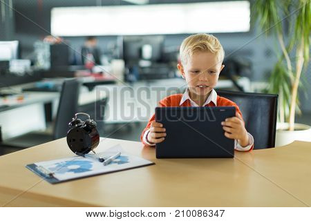 Cute Boy Sit At The Desk In The Office And Uses Tablet Pc