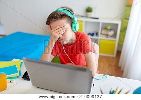 technology, gaming, cyberbullying and people concept - upset boy in headphones with laptop computer at home lost video game or suffer of bullying