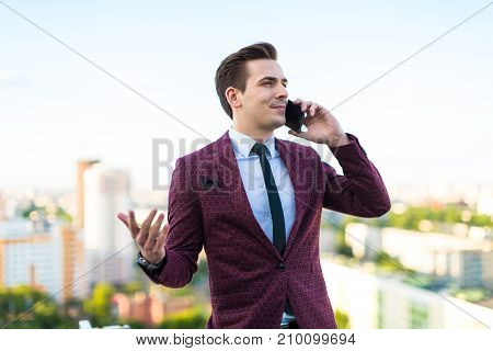 Young Serious Businessman In Red Suit And Shirt With Tie Stand On The Roof And Talk On The Phone