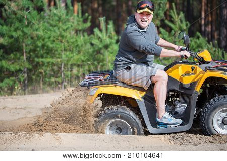 An Atv Quadbike Get Stuck In A Sandy Road Near Forest And Having Wheel-spin Making A Spray Of Sand