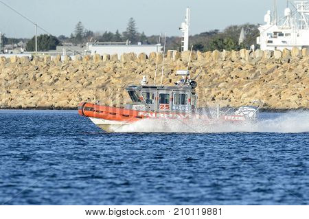 Fairhaven Massachusetts USA - October 20 2017: Fairhaven Fire Department 25-foot patrol boat throwing up spray with hurricane barrier in background