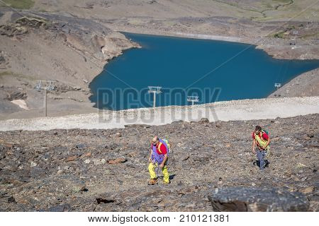 Two climbers with equipment walking to mountain in sunny day