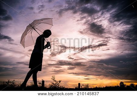 The sad girls silhouette style walking alone outdoor and umbrella in her hand with cloudy skies and evening sun