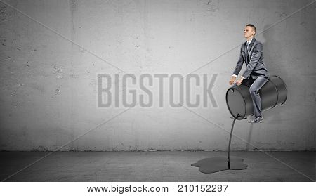 A small businessman sits on a black barrel leaking oil like on a horse. Oil industry king. Harness new venture. Petrol profits.