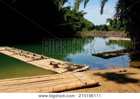 Traditional bamboo raft floats over the clear river in the morning with reflection of the forest and mountains
