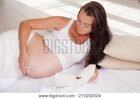 A Pregnant Woman Lies On A Bed And Reading A Book