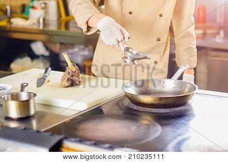 Chef pouring cooking oil into frying pan. Chef in restaurant going to cook the leg of lamb. European cuisine and cooking.