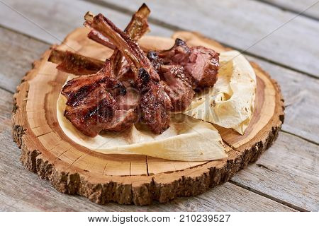 Appetizing roasted ribs calf on natural wood. Grilled ribs with lavash on wooden stand. Delicious meat on wooden table.