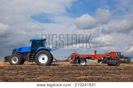 A Large Blue Tractor, Plowing Field Against The Beautiful Sky. Work Of Agricultural Machinery. Harve