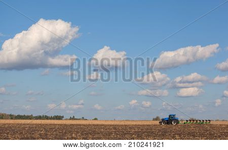 A Large Blue Tractor, Plowing Field Against The Beautiful Sky. Work Of Agricultural Machinery. Harve