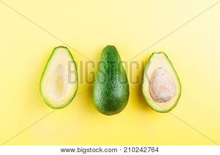 Aavocado and two halves in a row. Healthy living, diet, raw eating, vegetable fats concept. Avocado on the bright yellow background. Selective focus, space for text.