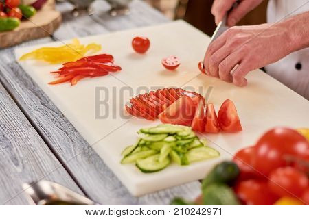 The process of cutting vegetables on white board. Male chef hands chopping fresh vegetables on cutting board. Chef working at professional kitchen.