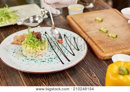 Chef serving salad with red caviar. Salad with herring in belgian style, avocado and toasts. Chef cooking dish at kitchen.