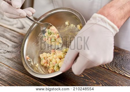 Chef stirring olivier salad in stainless bowl. Cook holding bowl with delicious olivier salad. Chef cooked traditional russian olivier salad.