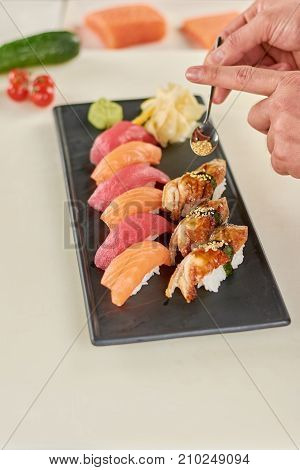Chef putting sesame on nigiri sushi. Cook preparing appetizing sushi at kitchen. Delicious sushi on plate.