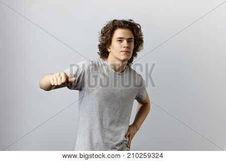 Picture of confident bigheaded young Caucasian man with curly hairstyle looking at camera with arrogant smile showing thumbs up gesture and pointing at himself. Confident self love and inflated ego