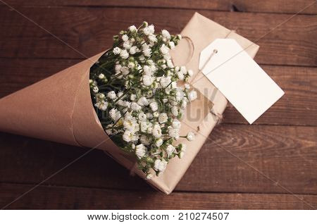 Bouquet of camomile field wrapped in kraft paper on a wooden table